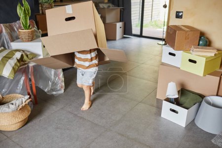 Foto de Retrato de lindo niño jugando con caja de cartón en la cabeza mientras la familia se muda a una casa nueva, espacio para copiar - Imagen libre de derechos