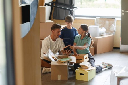 Photo for Candid portrait of happy family unpacking boxes sitting on floor while moving into new house, copy space - Royalty Free Image