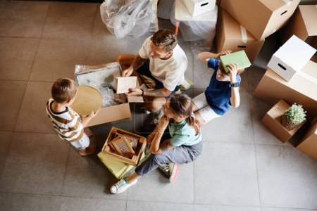 Foto de Retrato de vista superior de la familia con dos niños mudándose a una casa nueva y desempacando cajas juntos, espacio para copiar - Imagen libre de derechos