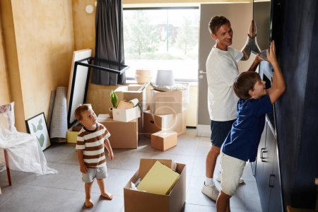 Foto de Retrato de vista lateral de padre e hijo sonrientes colgando TV en la pared mientras se mudan a una casa nueva, espacio para copiar - Imagen libre de derechos