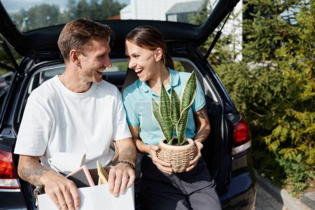 Téléchargez les photos : Portrait de couple adulte assis dans un coffre de voiture avec des boîtes et se regardant tout en déménageant dans une nouvelle maison - en image libre de droit