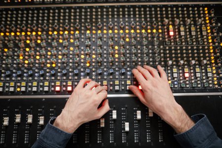 Photo for Top view background of male hands operating buttons and toggles at audio workstation in professional recording studio, music production theme - Royalty Free Image