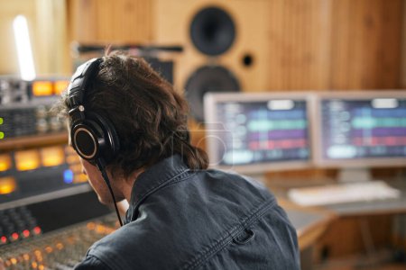 Photo for Male musician wearing headphones at audio workstation in professional recording studio, copy space - Royalty Free Image