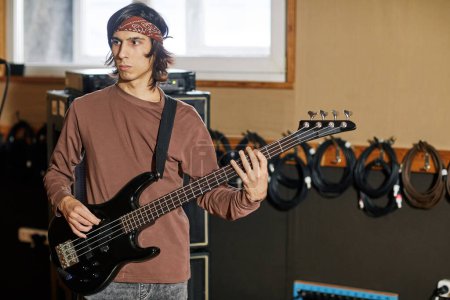 Photo for Waist up portrait of young musician playing bass guitar in recording studio, making rock music, copy space - Royalty Free Image