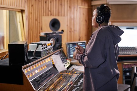 Side view portrait of female music producer showing thumbs up while supporting band in recording studio, copy space