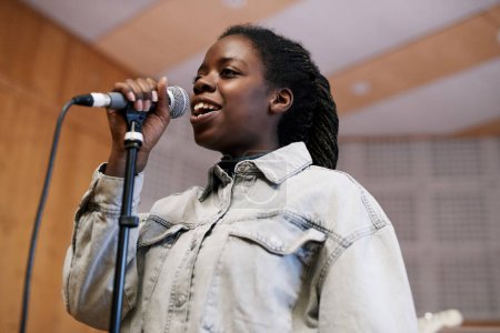 Photo for Low angle portrait of young black woman singing to microphone while recording music or rehearsing in professional studio - Royalty Free Image