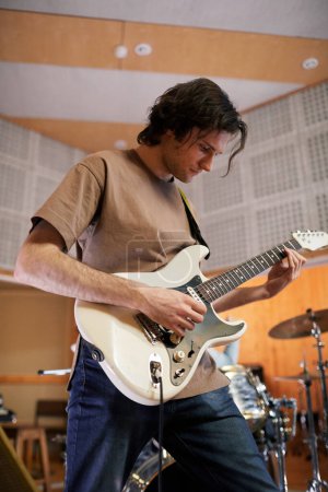Téléchargez les photos : Portrait en angle bas du jeune guitariste jouant de la musique dans un studio d'enregistrement professionnel - en image libre de droit