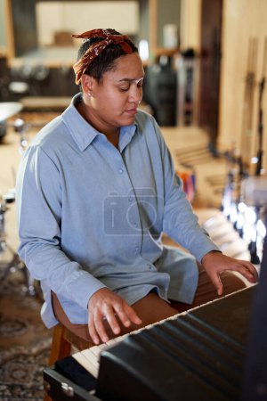 Photo for Vertical portrait of ethnic young woman playing keyboard while composing music in recording studio - Royalty Free Image