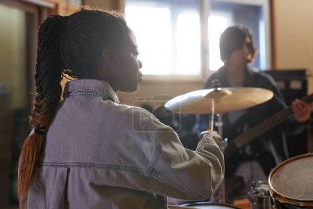 Foto de Vista posterior retrato de la joven baterista tocando música con la banda durante el ensayo en el estudio, espacio de copia - Imagen libre de derechos
