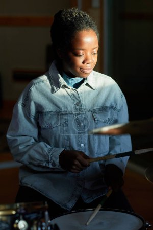 Photo for Vertical portrait of black young woman playing drums in dark with cinematic light accent - Royalty Free Image