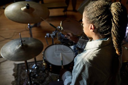 Téléchargez les photos : Portrait grand angle de jeune femme noire jouant de la batterie dans l'obscurité avec un accent léger, espace de copie - en image libre de droit