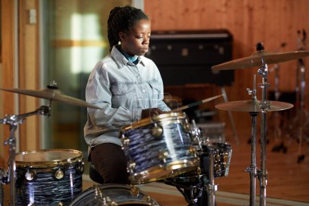 Photo for Portrait of black young woman playing drums alone while practicing in music studio with sun accent, copy space - Royalty Free Image