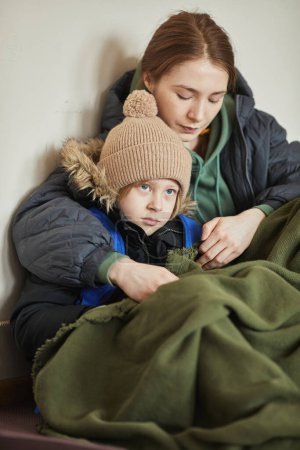 Photo for Vertical portrait of young Caucasian brother and sister hiding together in shelter during war crisis - Royalty Free Image
