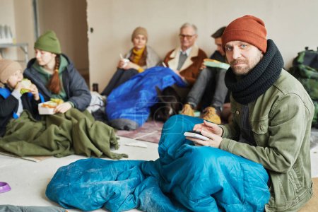 Téléchargez les photos : Portrait d'un homme caucasien se cachant dans un refuge pour réfugiés et regardant une caméra assis sur le sol recouvert d'une couverture, espace de copie - en image libre de droit