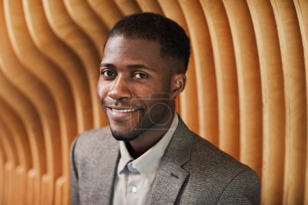 Téléchargez les photos : Portrait graphique d'un homme d'affaires noir souriant regardant une caméra dans un espace de bureau moderne avec lambris en bois, espace de copie - en image libre de droit