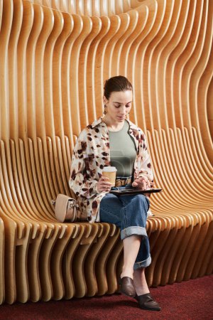 Foto de Retrato vertical de un joven profesional que usa tableta mientras trabaja en un espacio de oficina moderno con sillas de diseño - Imagen libre de derechos