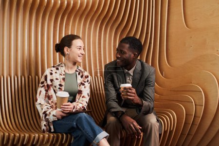 Téléchargez les photos : Portrait de jeunes collègues bavardant tout en se relaxant au salon dans un espace de bureau moderne avec des panneaux en bois - en image libre de droit