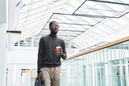 Foto de Retrato gráfico del joven hombre de negocios negro caminando en el edificio de oficinas mientras comienza a trabajar por la mañana, espacio para copiar - Imagen libre de derechos