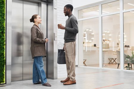 Photo for Full length portrait of two coworkers chatting by elevator in modern office building, copy space - Royalty Free Image