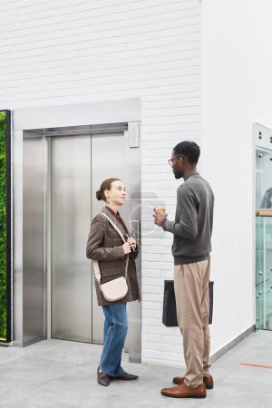 Photo for Vertical full length portrait of two coworkers chatting by elevator in modern office building - Royalty Free Image
