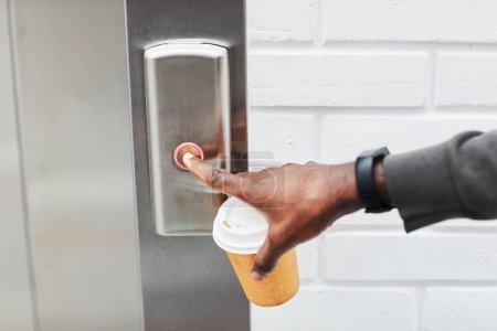 Foto de Primer plano del hombre negro anónimo presionando el botón del ascensor en la oficina y sosteniendo la taza de café, espacio para copiar - Imagen libre de derechos