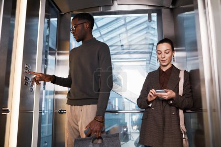 Photo for Front view of two young business people in glass elevator at modern office building, copy space - Royalty Free Image