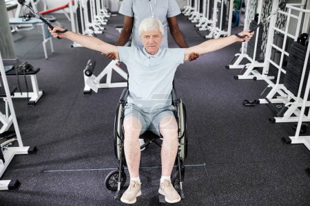 Téléchargez les photos : Portrait d'un homme âgé en fauteuil roulant faisant des exercices physiques au gymnase de la clinique de soins de santé - en image libre de droit