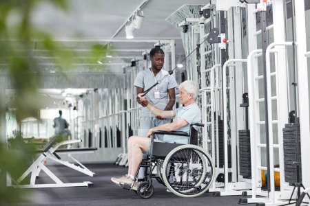 Side view portrait of senior man in wheelchair doing exercises in gym at rehabilitation clinic, copy space