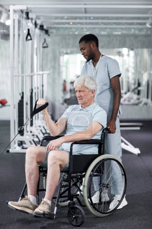Foto de Retrato completo del hombre mayor usando silla de ruedas en el gimnasio durante la terapia de rehabilitación en la clínica - Imagen libre de derechos
