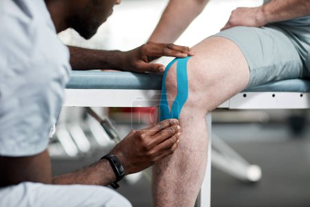 Photo for Close up of rehabilitation therapist using kinesio taping at knee of senior patient, copy space - Royalty Free Image
