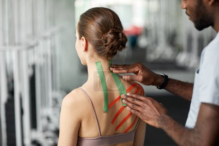 Foto de Primer plano del terapeuta poniendo cinta de kinesio en la espalda y el hombro de la mujer joven en la sesión de fisioterapia - Imagen libre de derechos