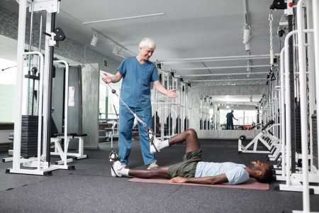 Photo for Side view portrait of physiotherapy specialist helping young man with rehabilitation exercises in gym, copy space - Royalty Free Image