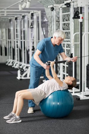 Full length portrait of senior rehabilitation therapist working with female patient at gym in clinic