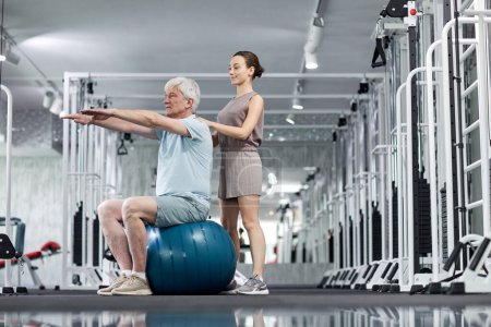 Foto de Retrato de vista lateral de una terapeuta joven que ayuda a un hombre mayor a hacer ejercicios en una clínica de rehabilitación, espacio para copiar - Imagen libre de derechos