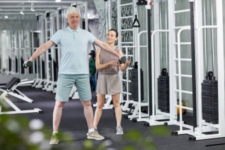 Foto de Retrato completo del hombre mayor haciendo ejercicios físicos en una clínica de rehabilitación con la ayuda de una terapeuta - Imagen libre de derechos