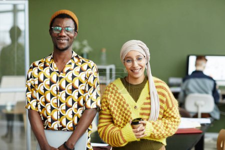 Photo for Waist up portrait of ethnic young couple wearing vibrant styles and smiling at camera in office - Royalty Free Image