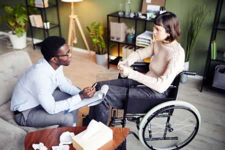 Foto de Mujer joven en silla de ruedas que tiene sesión de terapia privada con el psicólogo para aprender a aceptar la discapacidad - Imagen libre de derechos