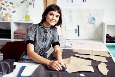 Photo for Smiling young seamstress outlining and cutting out garment details - Royalty Free Image