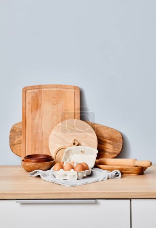 Photo for Image of kitchen table with wooden boards and fresh chicken eggs in basket against blue wall - Royalty Free Image