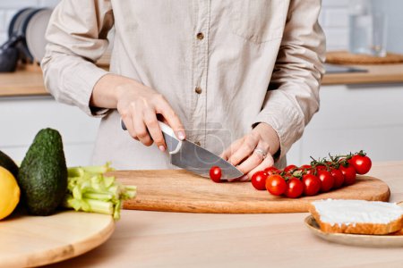 Foto de Primer plano de la joven mujer cortando tomates cherry con cuchillo en la tabla de cortar en la mesa de la cocina - Imagen libre de derechos