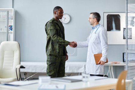 Photo for Young Black military officer wearing uniform and mature Caucasian doctor doing handshake after finishing consultation - Royalty Free Image