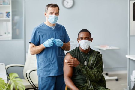 Photo for Portrait of mature male nurse holding syringe standing next to young Black military officer looking at camera after covid vaccination done - Royalty Free Image