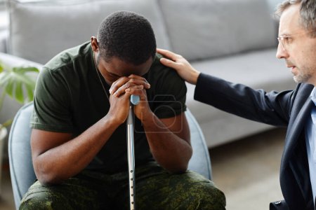 Téléchargez les photos : Psychologue mature réconfortant et soutenant soldat noir tout en traitant l'ESPT à la séance de thérapie - en image libre de droit