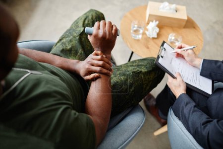 Photo for From above view shot of young adult Black soldier wearing military uniform sitting in psychologist office speaking about his depression - Royalty Free Image