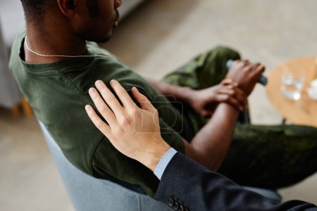Photo for High angle of Caucasian psychologist patting shoulder of Black soldier with PTSD to comfort him during therapy session - Royalty Free Image