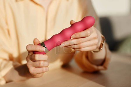 Téléchargez les photos : Minimal gros plan de la jeune femme tenant vibromasseur rose dans les mains tout en examinant les jouets sexuels, copier l'espace - en image libre de droit