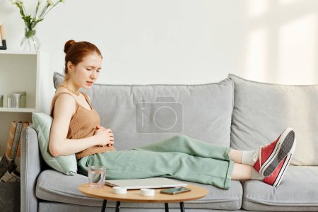 Téléchargez les photos : Portrait latéral de jeune femme souffrant de crampes d'époque couchée sur le canapé, espace de copie - en image libre de droit