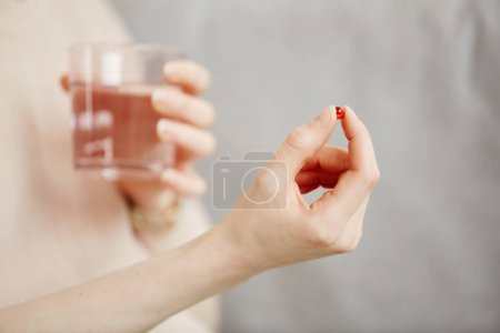 Photo for Minimal close up of young woman holding pill capsule and glass of water while taking medicine or vitamins, copy space - Royalty Free Image