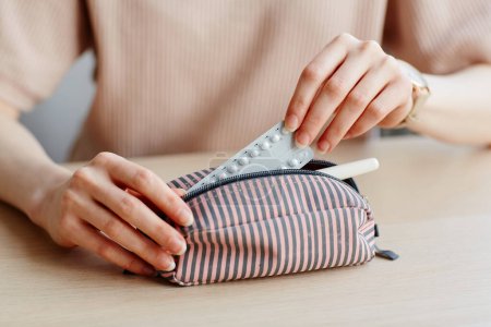 Photo for Minimal close up of young woman putting birth control pills in purse and other feminine essentials - Royalty Free Image