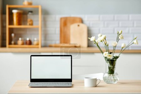Téléchargez les photos : Image de fond minimale de l'ordinateur portable ouvert avec écran blanc vierge sur une table en bois dans la cuisine décorée de fleurs fraîches au printemps, espace de copie - en image libre de droit